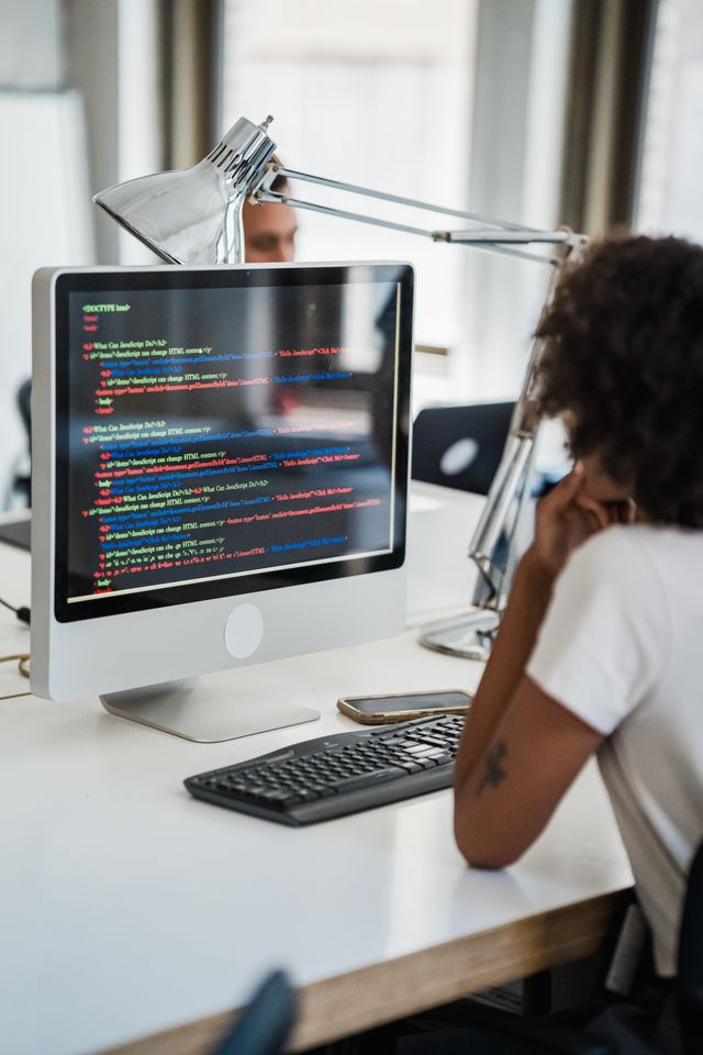 A female professional focused on coding at her office desk with a desktop computer.
