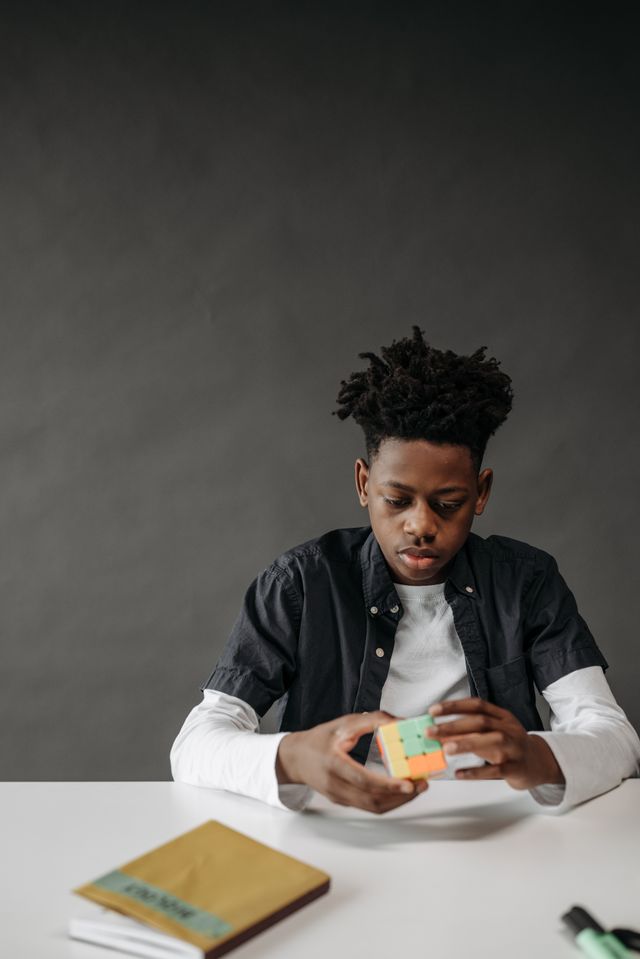 A focused young boy with dreadlocks solving a Rubik's cube in a studio setting.
